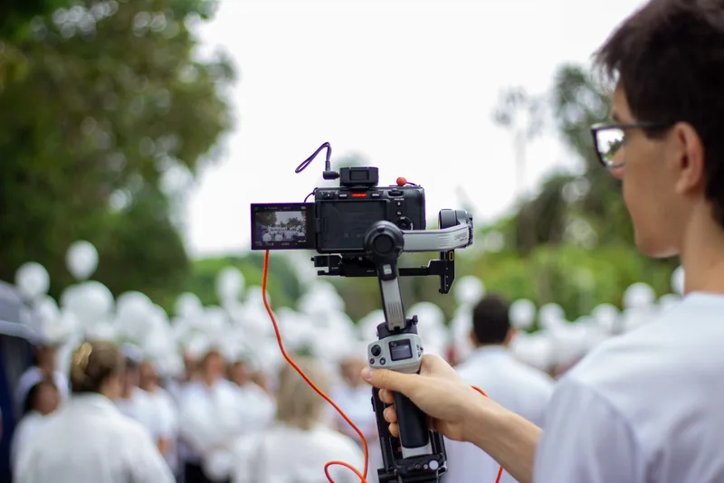 Câmera em gimbal filmando ao ar livre, com pessoas ao fundo